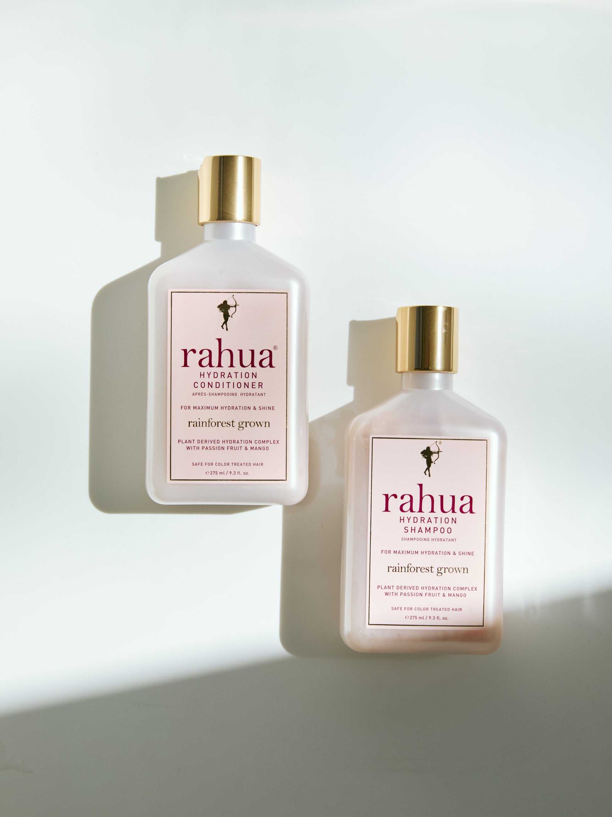 two bottles of rahua hair care hydration shampoo and conditioner plastic bottles with gold caps on a white background|variant:074-oz