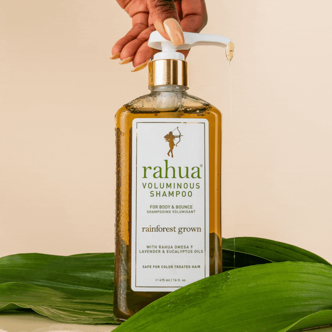 gif of plastic pump bottle with gold collar of 16 oz rahua voluminous shampoo model pumping out product of voluminous shampoo on a beige background with leaves on the floor|variant:16-oz