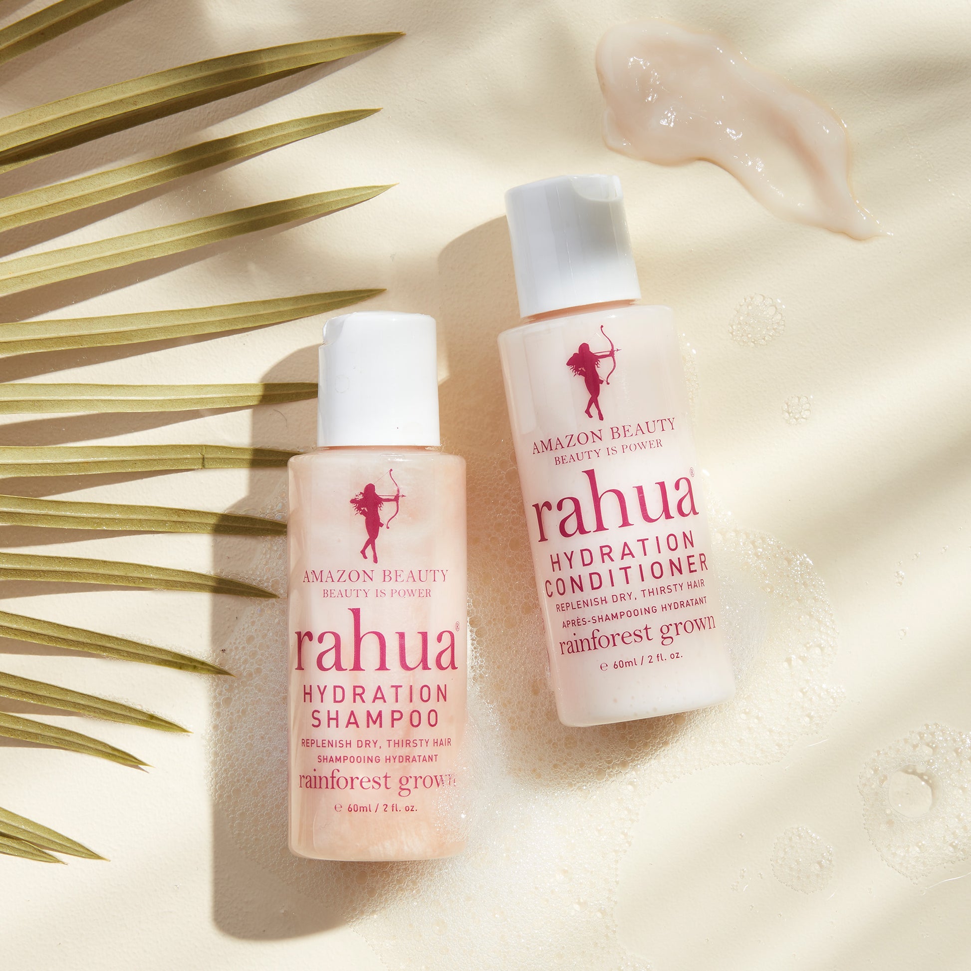 two bottles of travel size tsa friendly compliant rahua hydration conditioner and shampoo on a soapy beige background with a leaf on the left side|variant:2-oz