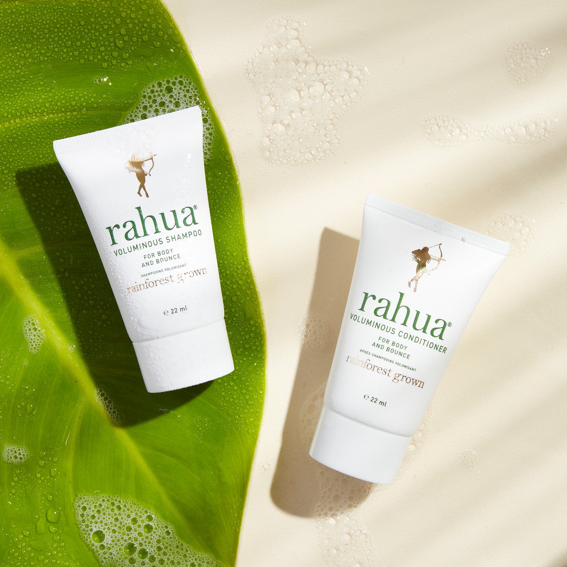 two tubes of rahua voluminous shampoo and voluminous conditioner with a palm leaf on a soapy beige background|variant:074-oz
