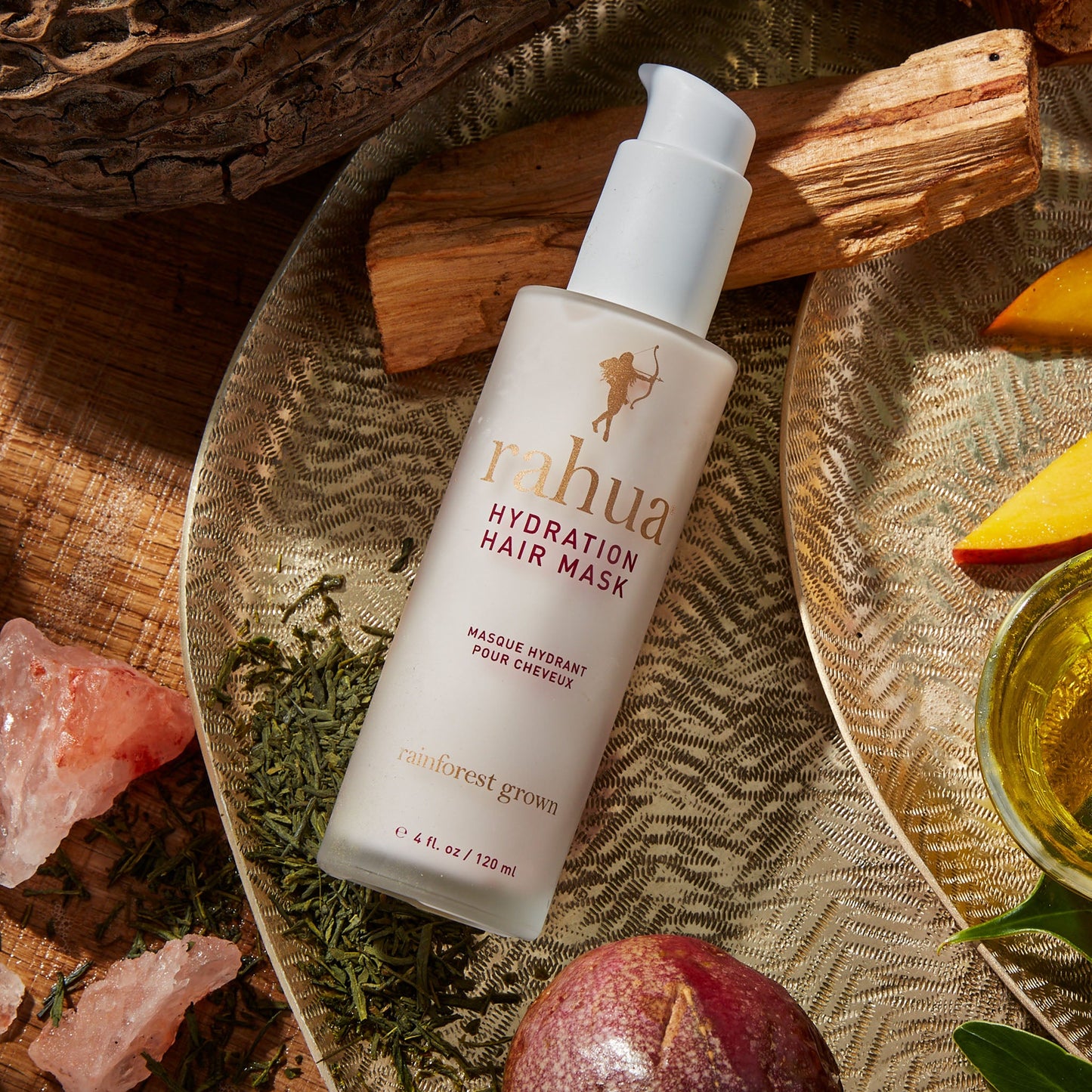 glass bottle of hydration hair mask on a golden plate resting on a wooden slab with passion fruit and mango in the background|variant:4-oz